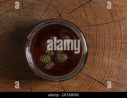 Marmelade aus grünen Kiefernzapfen im Glasbecher. Kiefernknospen in Honig. Kiefernknospen. Honig. Vegetarismus. Marmelade junger grüner Kiefernzapfen in einem Glasbecher. Draufsicht. Stockfoto
