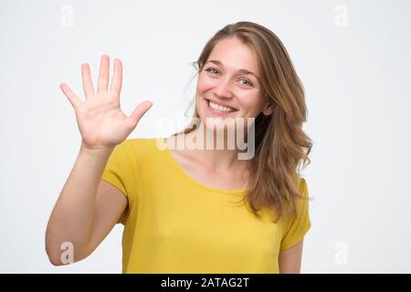 Attraktive, freundlich aussehende junge Frau lächelt fröhlich und zeigt fünf Finger. Studio gedreht Stockfoto