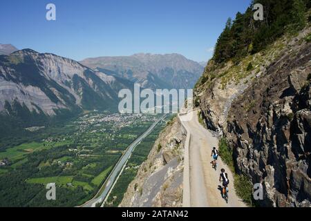 LUFTAUFNAHME von einem 6 m hohen Mast. Radfahrer auf einer schmalen Straße über einem steilen Berghang. Auris Road, oberhalb von Le Bourg d'Oisans, Frankreich. Stockfoto