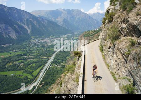 LUFTAUFNAHME von einem 6 m hohen Mast. Radfahrer auf einer schmalen Straße über einem steilen Berghang. Auris Road, oberhalb von Le Bourg d'Oisans, Frankreich. Stockfoto