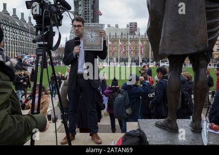 Ein französischer TV-Reporter steht neben der Statue von Mahatma Gandhi und hält die Titelseite der Zeitung Times mit der Seite ein Bild von Big Ben, am Brexit Day, dem Tag, an dem Großbritannien die Europäische Union am 31. Januar 2020 rechtskräftig verlässt, in Westminster auf. In London, England. Stockfoto