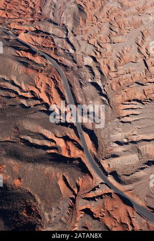 LUFTAUFNAHME. Kurvenreiche Straße in einer Landschaft aus roten und grauen Badlands. Süd-Nevada, USA. Stockfoto