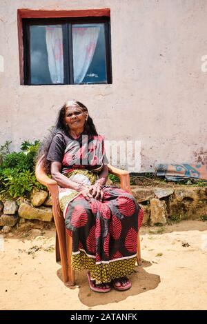 Alte Frau, die auf einem Stuhl vor ihrem Haus in Sri Lanka sitzt Stockfoto