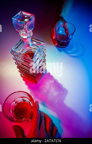Glaskaraffe mit zwei Glasgläsern. Zwei Personen trinken von oben aus Alkohol Stockfoto