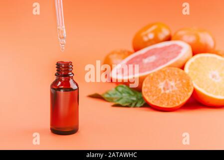 Frische reife Mandarinen, Grapefruit und Orangen mit grünen Blättern und Glasflasche mit ätherischem Öl auf orangefarbenem Hintergrund. Stockfoto