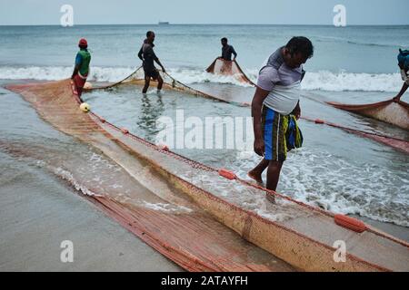 Fischer ziehen die Netze am Strand in Sri Lanka aus dem Meer. Die Stadt Trincomalee hat einen großen und langen Strand, an dem die Einheimischen Netze und Fische ziehen. Stockfoto