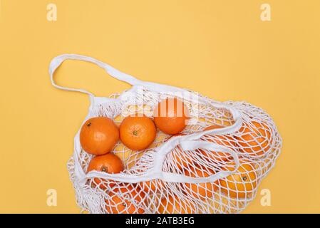 Zusammensetzung mit Mandarinen in einem Saitenbeutel auf orangefarbenem Hintergrund. Stockfoto