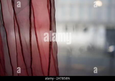 Roter Vorhang am Fenster, halb eingezogen - innen Stockfoto