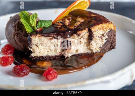 Schokoladendessert mit einer Schaufel Kaffeeissahne, Scheiben getrockneter Kirsche und einer Scheibe Orange. Garniert mit Minzblättern. Cappuccino im Backgr Stockfoto