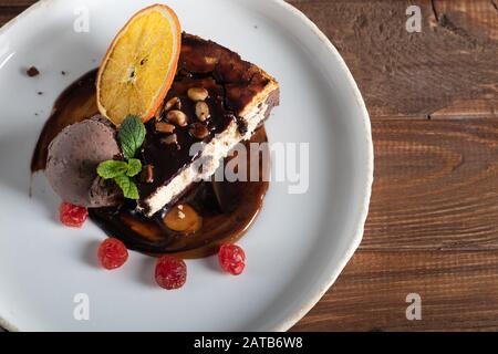 Schokoladendessert mit einer Schaufel Kaffeeissahne, Scheiben getrockneter Kirsche und einer Scheibe Orange. Garniert mit Minzblättern. Cappuccino im Backgr Stockfoto