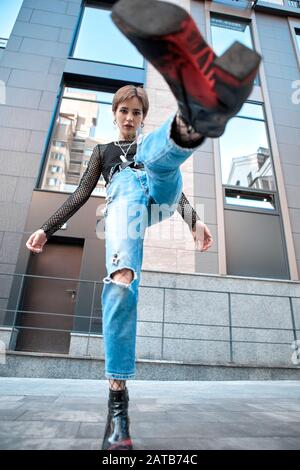 Urbaner Stil. Junge, stilvolle Frau, die in der Nähe des Wolkenkratzers ein Bein hoch steht und die Bodenansicht kühl stellt Stockfoto