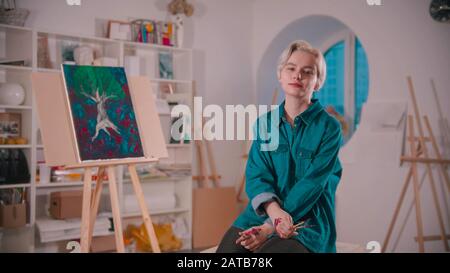 Eine junge Künstlerin mit kurzen blonden Haaren sitzt im Kunststudio Stockfoto