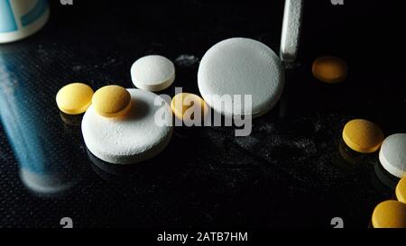 Pharma- und Medizinkonzept auf schwarzem Hintergrund. Medizinische Pillen. Medikamente und Medikamente. Viele Tabletten gelbe Tabletten und weiße Kapseln Stockfoto