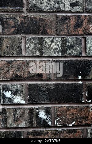 Eine reich dunkle, mehrfarbige, gesättigte und verwitterte Ziegelwand, nah oben, mit einem lebhaften diagonalen weißen Fleck; Hintergrund. Stockfoto