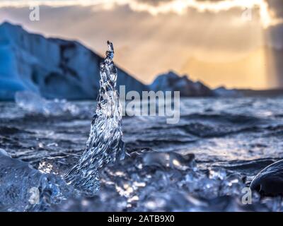 Ein Eiskristall ragt aus dem Wasser empor. Im Hintergrund bildet der versteckte Sonnenuntergang den perfecten Kontrast. Ein romantischer Moment. Stockfoto