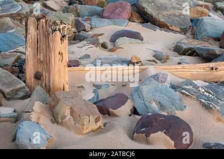 Alter Pfosten und Treibholz verwitterten zwischen Felsen im Sand am Crow Point Beach, Devon Stockfoto