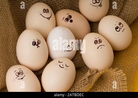 Lustige Eier mit gemalten Gesichtern, die unterschiedliche Emotionen auf einem rustikalen Burlock ausdrücken. Fröhliches Osterkonzept Stockfoto