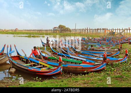 Bunte traditionelle Boote auf der Seite des Taung Tha Man Lake, in der Nähe von Mandalay, Myanmar, umgeben von grüner Vegetation, gegen einen klaren Himmel bedeckt Stockfoto