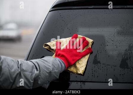 Der Mann hält die Mikrofaser in der Hand und poliert den Glaswagen. Stockfoto