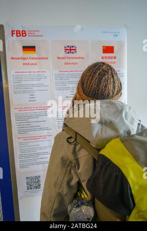 Flughafen Berlin-Schönefeld SXF, Deutschland - 02/01/20: Ein Mädchen mit Tasche liest im Flughafenterminal ein Warnschild über Coronavirus 2019-nCoV. Geschrieben Stockfoto