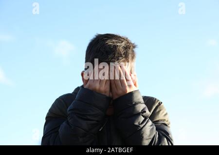 Ein 12-jähriger Junge bedeckt sein schlammiges Gesicht mit den Händen und blickt auf die Kamera Stockfoto