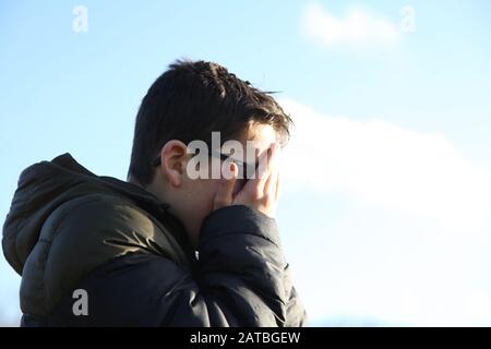 Ein 12-jähriger Junge bedeckt sein schlammiges Gesicht mit den Händen und dem Seitenprofil Stockfoto