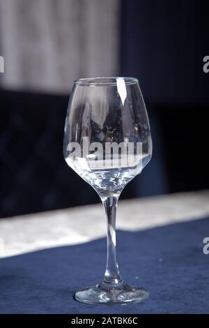 Geschirr auf dem Tisch im Café, Schwerpunkt auf Wineglasstamm. Elegante Tischeinstellung . Bakalblauer Hintergrund. Leeres Weinglas. Stockfoto