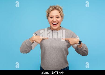 Das bin ich! Staunende egoistische Frau mit kurzen lockigen Haaren im Sweatshirt, die sich selbst zeigt und Verwunderung zum Ausdruck bringt, überrascht von persönlicher Leistung Stockfoto