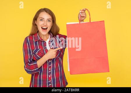 Verblüffte shopaholische, aufgeregte Ingwer-Mädchen in legeren Hemden, die mit schockierter Ausdrucksweise auf Einkaufstaschen zeigen, überrascht von Rabatten, gelungener Kauf. Stockfoto