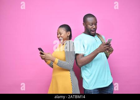 Aufgeregte junge schwarze Leute, die sich zurücklehnen, um Inhalte auf ihrem Handy zu sehen, sehen überrascht aus, junger afrikanischer Mann und Frau Stockfoto