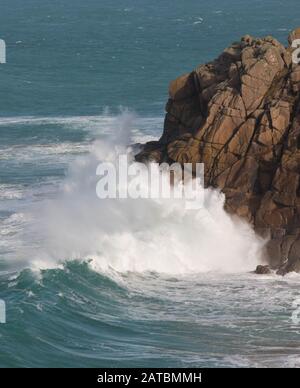 Wellen, die auf Felsen mit blauem Himmel in Pendeen, Cornwall abstürzen Stockfoto