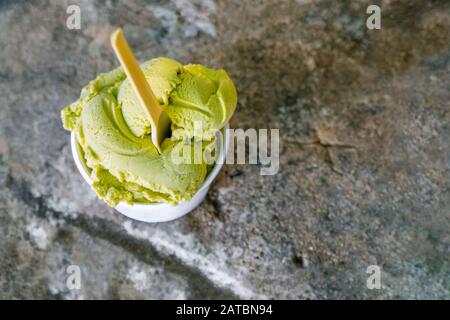Pistazieneis auf grauem Steingrund. Hausgemachtes Pistazieneis in klassischer Schüssel auf grauem Betontisch mit Draufsicht. Matcha Eiscreme in Schüssel auf grauem Steingrund Stockfoto