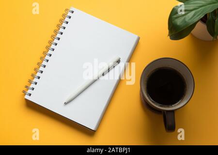 Stock-Foto einer leeren, geöffneten Notizbuchseite mit Bleistift, Kaffee und einer Pflanze auf gelbem Hintergrund Stockfoto