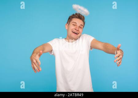 Lassen Sie mich Sie umarmen! Engeliger gutherziger Mann mit Halo über Kopf, der die Hände ausstreckt, um zu umarmen und Kamera mit kindlichem fröhlichem Ausdruck anzuschauen. In Stockfoto