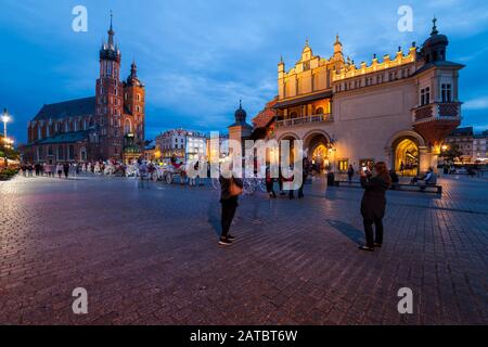 Krakow, Polen - 23. September 2018: Menschen und Pferdekutschen am Hauptplatz in der Altstadt, historisches Zentrum bei Abenddämmerung mit S Stockfoto