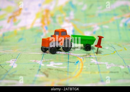 Der orangefarbene Traktor bewegt sich zum Hof. Ein Spielzeugschlepper befindet sich auf einer Karte. Das Konzept der Landwirtschaft. Stockfoto