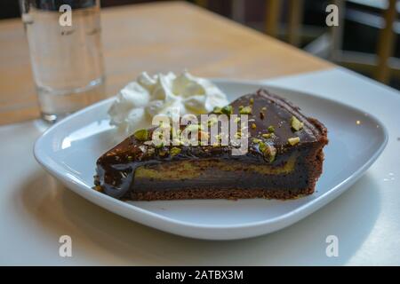 Ein köstliches Stück dunkle Schokolade und Pistacchio Kuchen. Ein Gourmet-Genuss für einen besonderen Tag. Eine cremige Füllung mit Dekoration aus Pistacchio zerbröckelt. Fre Stockfoto