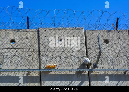 Eine Nahaufnahme der Trennmauer aus grauem Beton zwischen Israel und Palästina. Eine Kugel und eine Flasche von Kindern im Westjordanland fingen im Stacheldraht Stockfoto