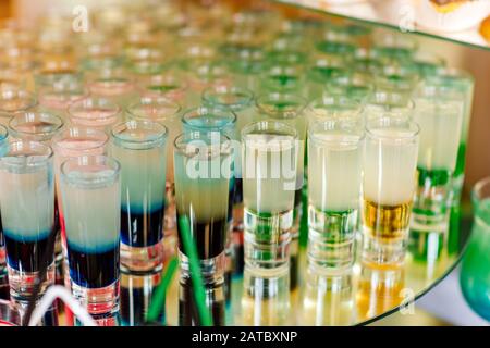 Viele verschiedene bunte Alkoholische schossen Cocktails in Trinkgläsern grün braun rot und weiß, die auf dem Spiegeltisch an der Bar stehen. Alkoholset Stockfoto