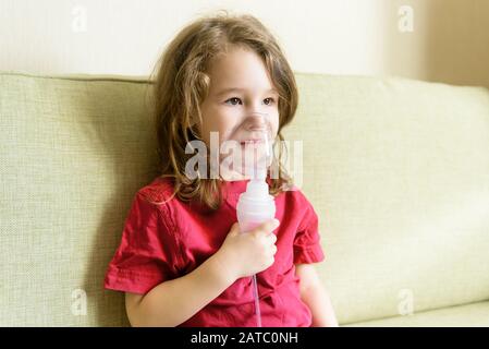 Kleines Mädchen hält Inhalationsmaske zu Hause. Krankes Kind atmet durch einen Vernebler. Baby mit Geräten zur Behandlung von Asthma oder Bronchitis. Konzept der Behandlung Stockfoto