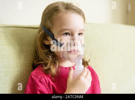 Kleines Mädchen hält Inhalationsmaske zu Hause. Krankes Kind atmet durch einen Vernebler. Baby mit Geräten zur Behandlung von Asthma oder Bronchitis. Konzept der Behandlung Stockfoto