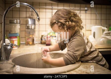 Ein süßes zweijähriges Mädchen wäscht in der Küche Geschirr Stockfoto