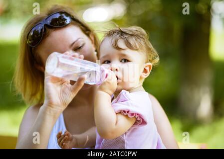 Die Mutter schenkt ihrem Mädchen Wasser aus einer Flasche in einem Park. Ein Jahr Kind im Freien. Stockfoto