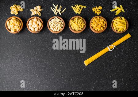 Auswahl verschiedener trockener Nudelsorten vor schwarzem Hintergrund, Draufsicht. Stockfoto