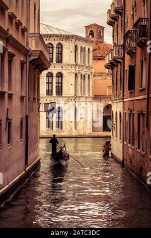 Die Gondel mit Touristen schwimmt entlang des schmalen Kanals in Venedig, Italien. Die Gondel ist der attraktivste Touristentransport Venedigs. Stockfoto