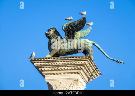 Die berühmte alte geflügelte Löwenskulptur auf der Piazza San Marco am blauen Himmelshintergrund in Venedig, Italien. Der Löwe ist ein Symbol Venedigs. Stockfoto
