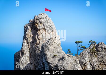 Der Felsen auf dem Berg Ai-Petri mit roter Flagge und Bäumen über dem Schwarzen Meer auf der Krim, Russland. Ai-Petri ist eines der höchsten Berge der Krim und Touristen Stockfoto