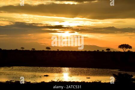 Ein wunderschöner afrikanischer Sonnenuntergang mit leuchtenden Farben, der in einem kleinen Teich in einem Nationalpark in Kenia reflektiert wird Stockfoto