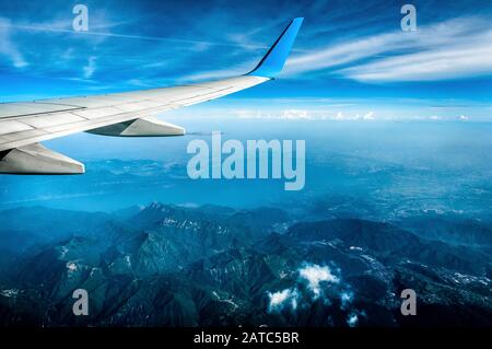 Flugzeugflügel über Alpen. Der Flügel des Flugzeugs auf blauem Himmel und Erdhintergrund. Flug über die Alpenlandschaft. Luftpanorama von Land und Stockfoto