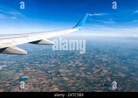 Flügel eines Flugzeugs über Dörfer oder die Landschaft fliegen. Der ebene Tragfläche auf den blauen Himmel und Erde Hintergrund. Antenne Panoramablick auf motley Land Stockfoto